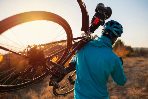 Rear view of a mountain biker carrying a bicycle on his shoulder over the nature trail.